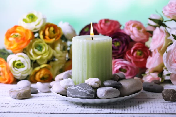 Composição com pedras de spa, vela e flores na mesa de madeira cor, no fundo claro — Fotografia de Stock