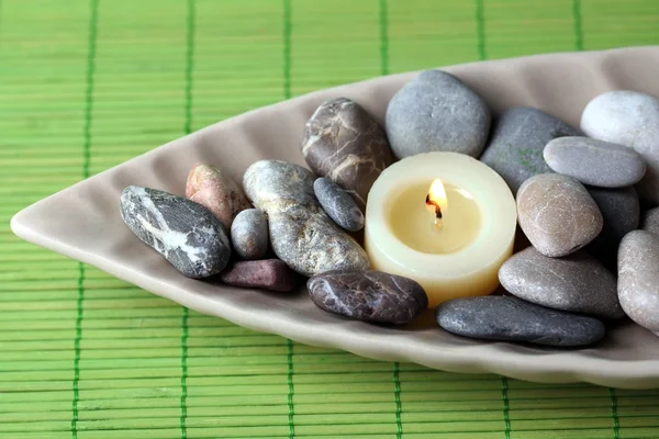 Wellness-Steine und Kerze in dekorativer Schale, auf Korbmatte Hintergrund — Stockfoto