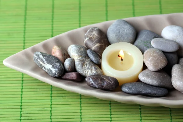 Pedras de spa e vela em tigela decorativa, no fundo esteira de vime — Fotografia de Stock