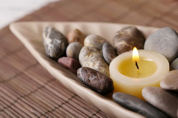 Spa stones and candle in decorative bowl, on bamboo mat, on color wooden table, on bright background — Stock Photo, Image