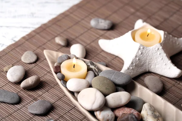 Composizione con pietre termali, candele su sfondo tappetino di bambù — Foto Stock