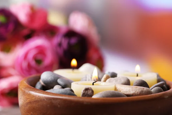 Композиція з спа-камінцями, свічками та квітами на бамбуковому килимку, на яскравому фоні — стокове фото