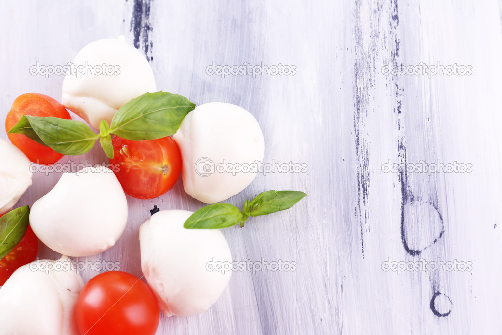 Tasty mozzarella cheese with basil and tomatoes, on wooden table