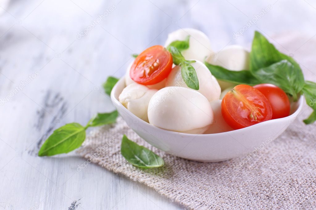 Tasty mozzarella cheese with basil and tomatoes in bowl, on wooden table