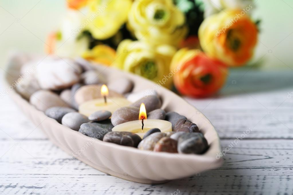 Composition with spa stones, candles  and flowers on color wooden table, on light background