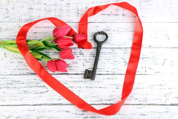 Key to love and happiness. Composition with key, ribbon and flowers. Conceptual photo. On color wooden background — Stock Photo, Image