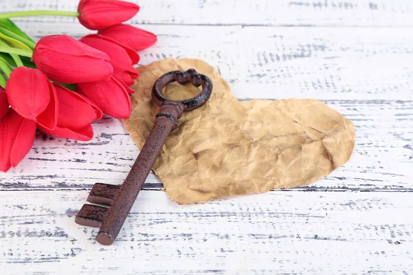 Clave para el amor y la felicidad. Composición con llave, corazón de papel y flores. Foto conceptual. Sobre fondo de madera de color — Foto de Stock