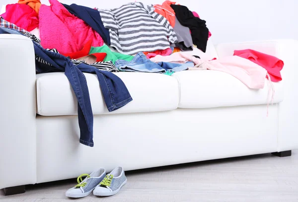 Messy colorful clothing on white sofa on white wall background — Stock Photo, Image