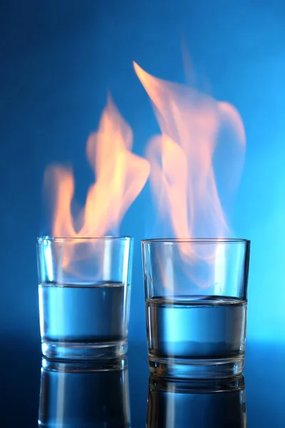 Glasses with burning alcohol on blue background — Stock Photo, Image