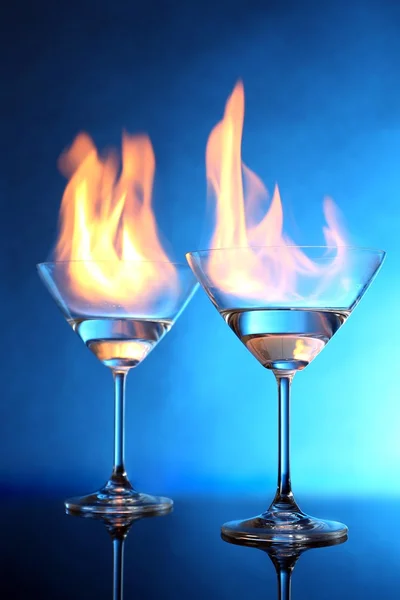 Glasses with burning alcohol on blue background — Stock Photo, Image