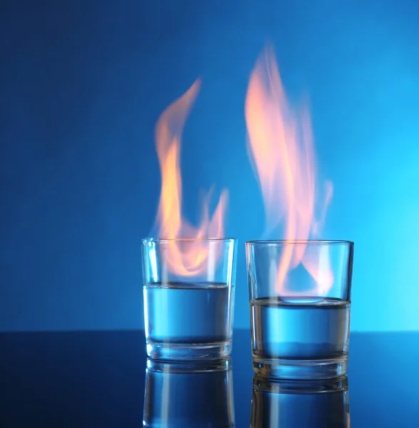 Glasses with burning alcohol on blue background — Stock Photo, Image