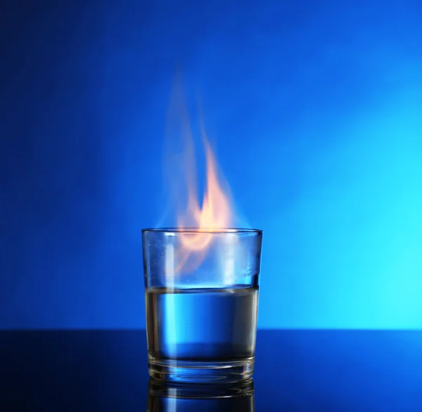 Vidro com álcool em chamas no fundo azul — Fotografia de Stock