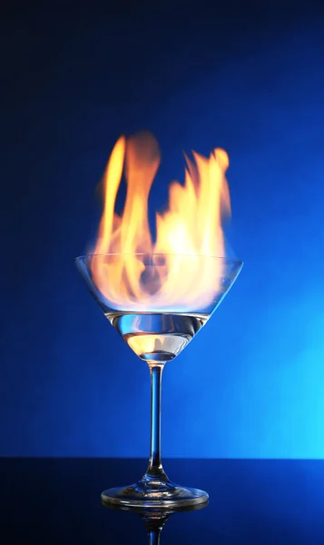 Bicchiere con alcool bruciante su sfondo blu — Foto Stock