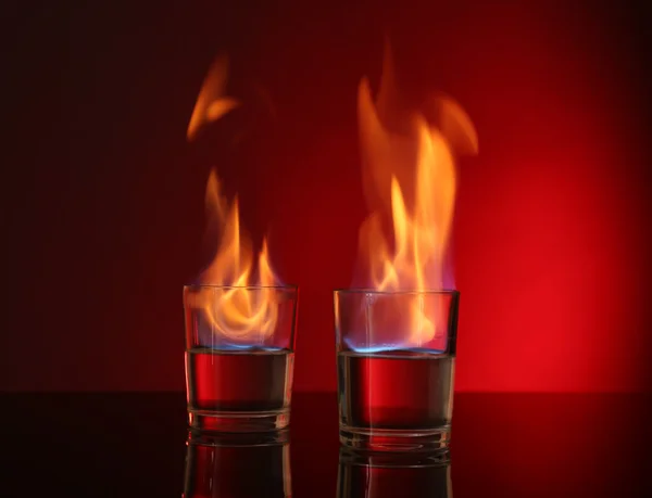 Glasses with burning alcohol on red background — Stock Photo, Image