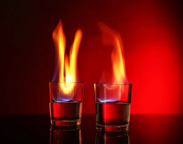 Glasses with burning alcohol on red background — Stock Photo, Image