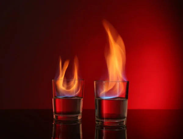 Gafas con alcohol quemado sobre fondo rojo — Foto de Stock