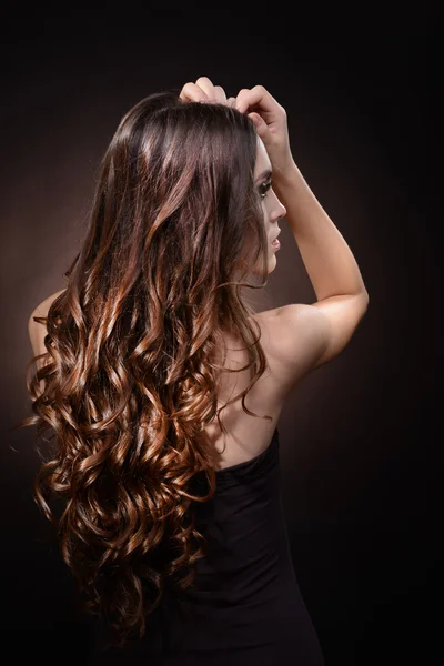Gyönyörű fiatal nő, hosszú haj, sötét barna háttér — Stock Fotó