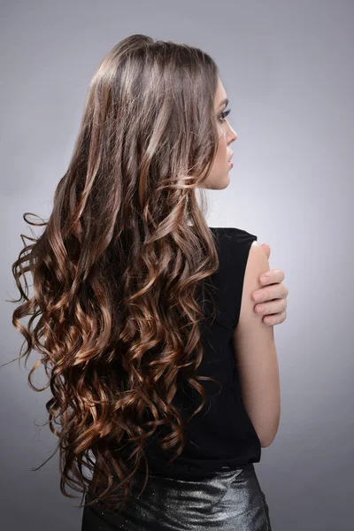 Schöne junge Frau mit langen Haaren auf grauem Hintergrund — Stockfoto