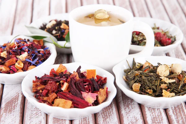 Xícara de chá com chá seco aromático em tigelas em fundo de madeira — Fotografia de Stock
