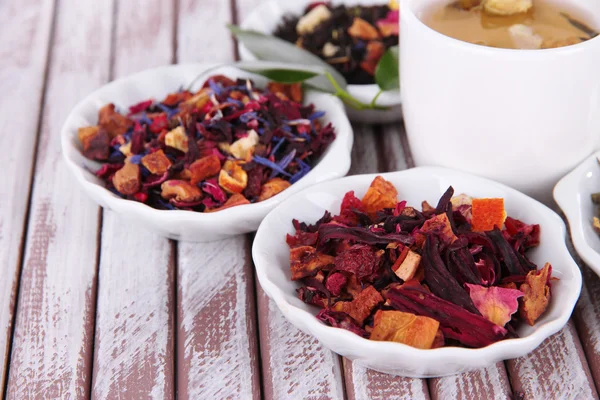 Tasse Tee mit aromatischem, trockenem Tee in Schalen auf Holzgrund — Stockfoto