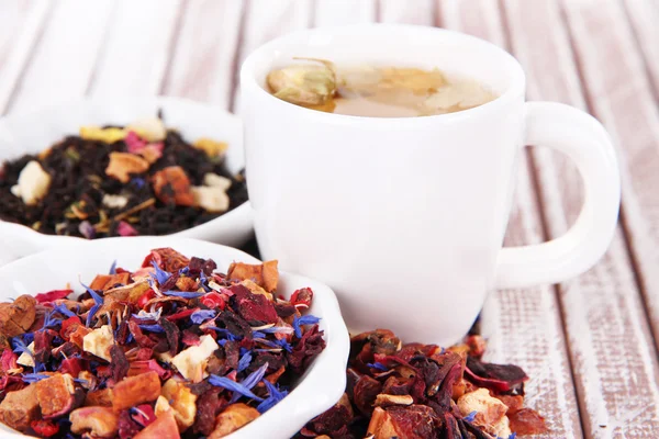 Tasse Tee mit aromatischem, trockenem Tee in Schalen auf Holzgrund — Stockfoto