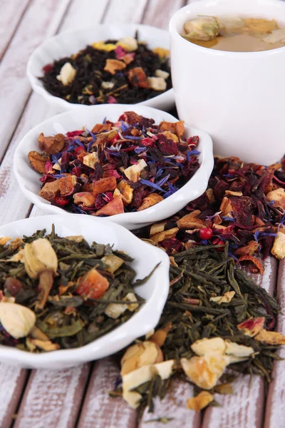 Kopje thee met aromatische droge thee in kommen op houten achtergrond — Stockfoto