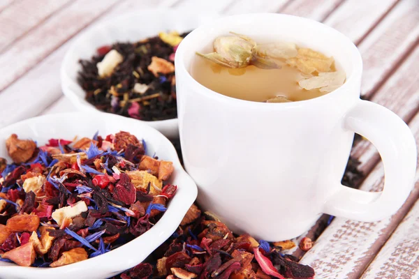 Чашка чаю з ароматним сухим чаєм в мисках на дерев'яному фоні — стокове фото