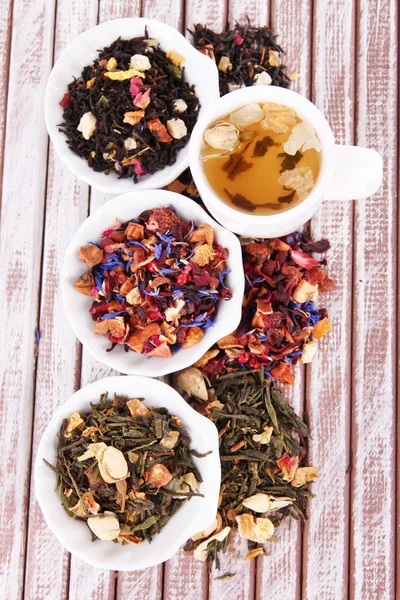 Tazza di tè con tè aromatico secco in ciotole su fondo di legno — Foto Stock