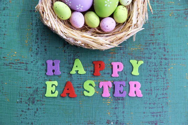 Easter eggs in nest and sign on color wooden background — Stock Photo, Image