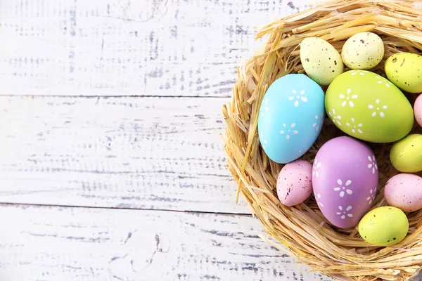 Easter eggs in nest on color wooden background — Stock Photo, Image