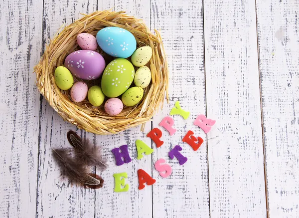 Uova di Pasqua nel nido e segno su sfondo di legno a colori — Foto Stock