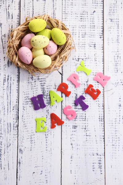 Easter eggs in nest and sign on color wooden background — Stock Photo, Image