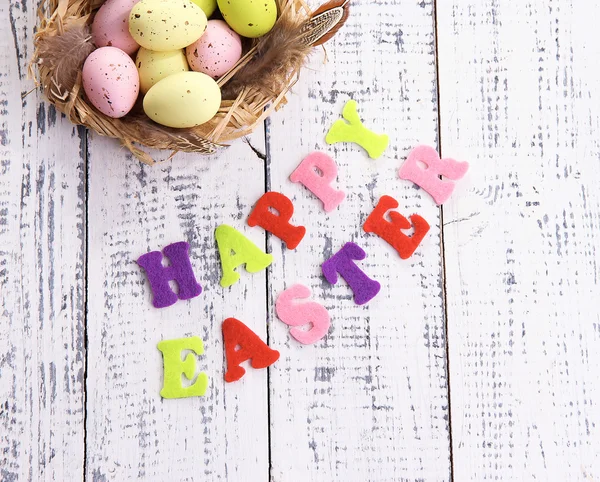 Easter eggs in nest and sign on color wooden background — Stock Photo, Image