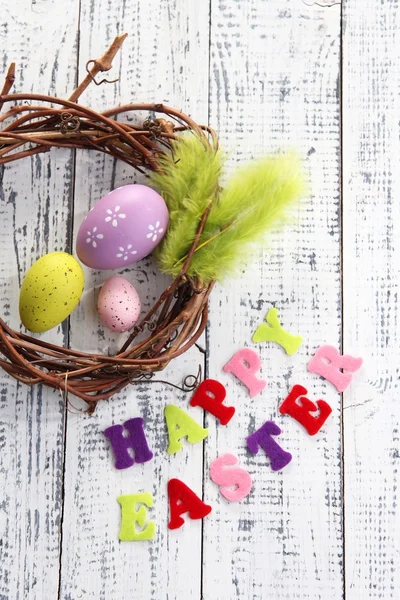 Composition with wreath, feathers, Easter eggs  on color wooden background — Stock Photo, Image