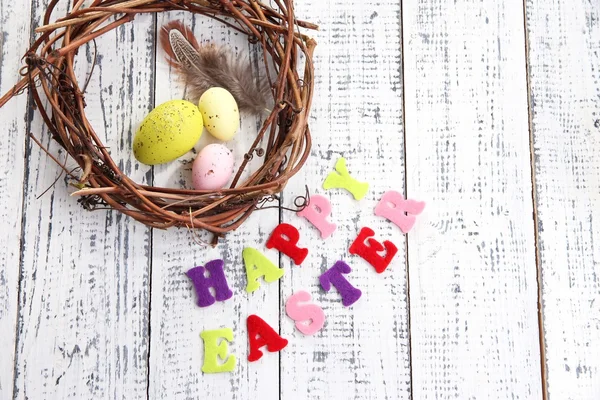 Composition with wreath, feathers, Easter eggs  on color wooden background — Stock Photo, Image