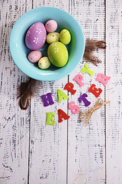 Huevos de Pascua en cuenco de color, plumas y letrero sobre fondo de madera color —  Fotos de Stock