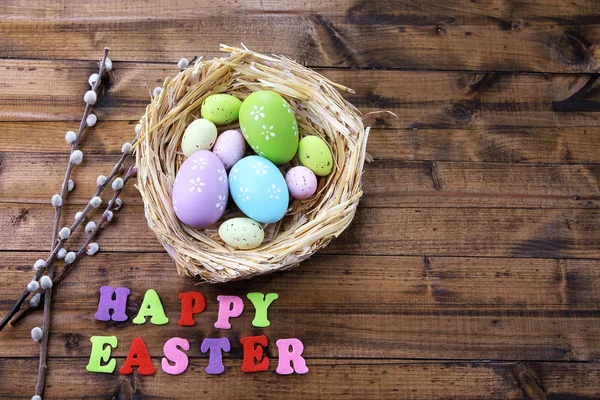 Пасхальные яйца в гнезде, киска-ива и знак на цветном деревянном фоне — стоковое фото
