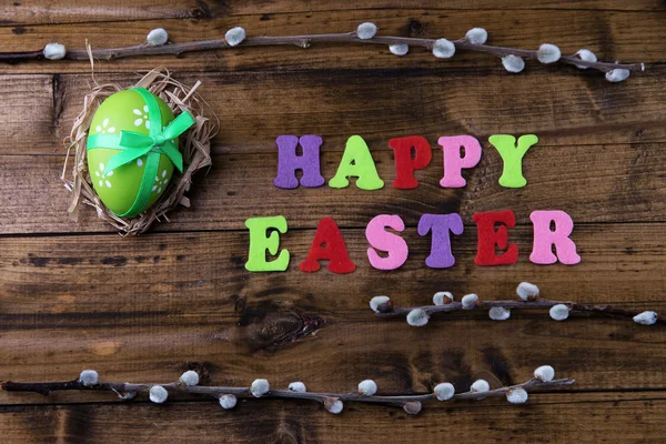 Easter egg in nest, pussy-willow and sign on color wooden background — Stock Photo, Image