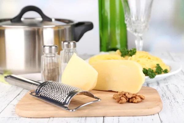 Composizione con gustosi spaghetti, grattugia, formaggio, bottiglia di vino e bicchiere su tavola di legno, su fondo chiaro — Foto Stock