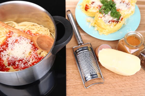 Composition with tasty spaghetti in pan, grater, cheese, on wooden table background — Stock Photo, Image