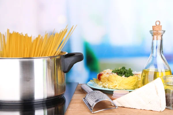 Processus de préparation des pâtes. Composition avec spaghettis en rangée dans une casserole, râpe, fromage, sur une table en bois sur fond lumineux — Photo