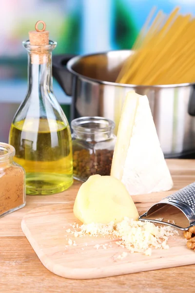 Process of preparing pasta. Composition with row spaghetti in pan, grater, cheese, on wooden table  on bright background — Stock Photo, Image