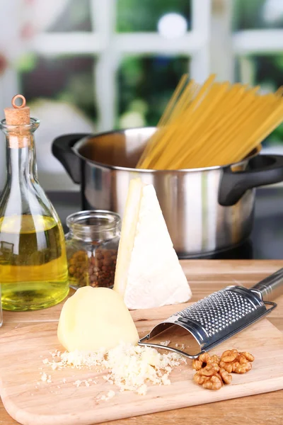 Η διαδικασία της προετοιμασίας των ζυμαρικών. σύνθεση με σειρά σπαγγέτι στο τηγάνι, τρίφτη, τυρί, σε ξύλινο τραπέζι σε φωτεινό φόντο — Φωτογραφία Αρχείου