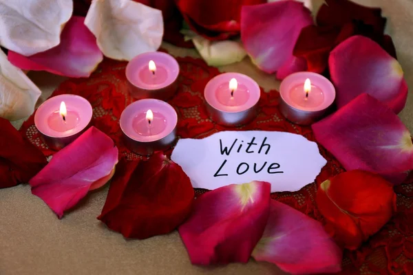 Piękne czerwone płatki róż z świece i kartkę z życzeniami, z bliska — Zdjęcie stockowe