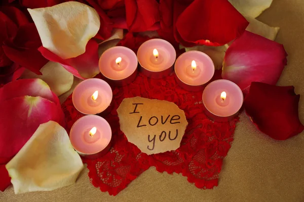 Bellissimi petali di rosa rossa con candele e biglietto di auguri, da vicino — Foto Stock
