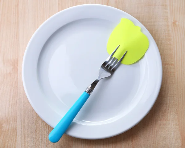 Carta a note vuote attaccata alla forchetta, su piatto, su sfondo di legno a colori — Foto Stock