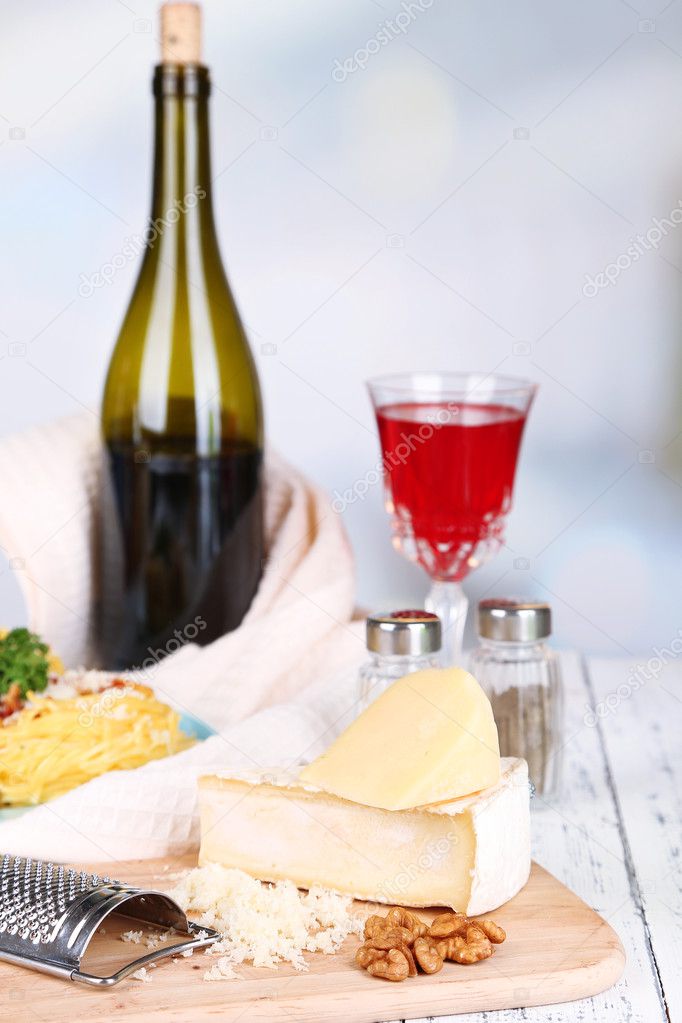Composition with tasty spaghetti, cheese, wine bottle and glass on wooden table, on light background