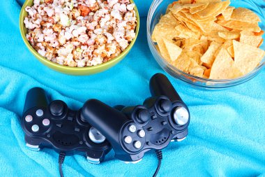 siyah oyun denetleyicileri ve aperatifler renkli kareli arka plan üzerine bir kase