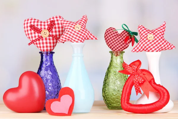 Hand-made textile hearts in different vases on wooden table, on light background — Stock Photo, Image