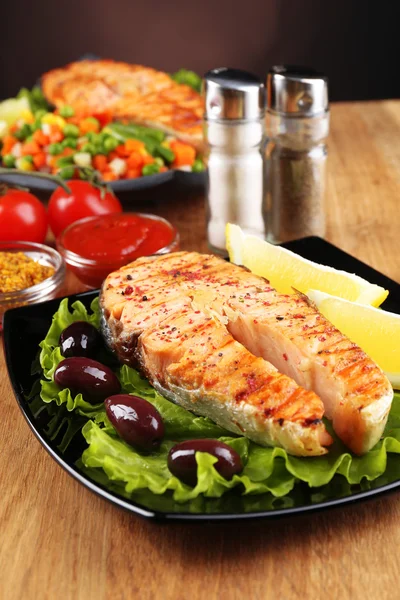 Tasty grilled salmon with lemon and vegetables, on wooden table — Stock Photo, Image